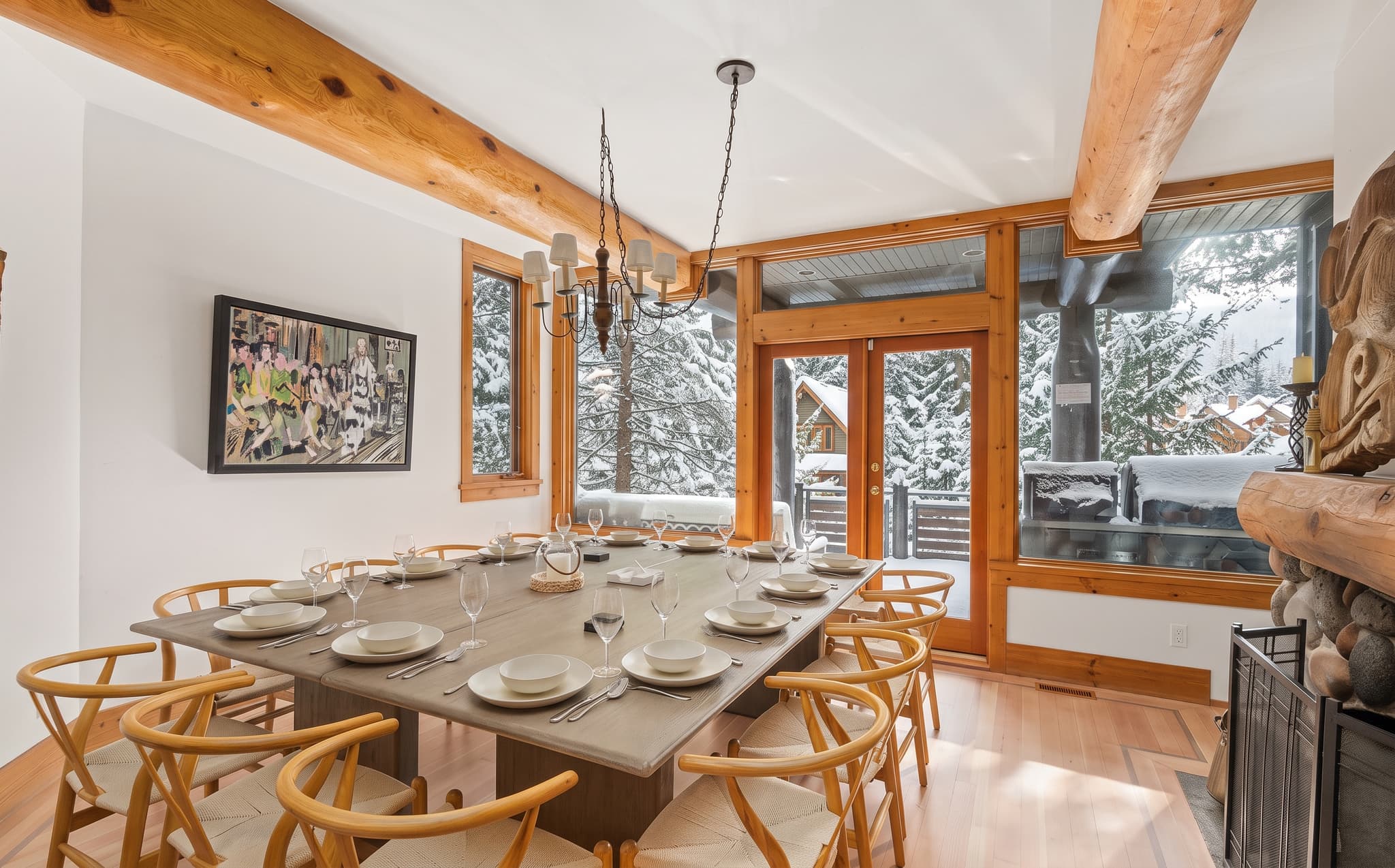Long dining table set for a group meal in a Whistler chalet with snowy trees outside the windows