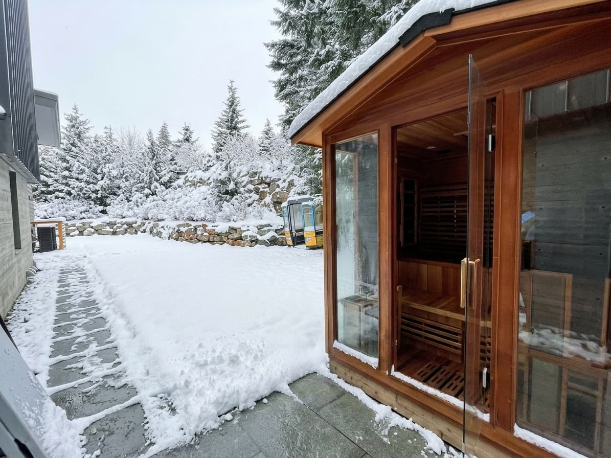 Cedar outdoor sauna beside a snow-covered patio and forest at a Whistler home